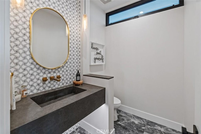 half bathroom featuring marble finish floor, a sink, toilet, and baseboards