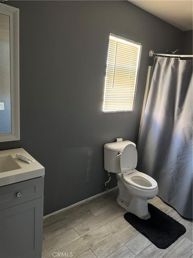 full bath featuring wood finish floors, baseboards, vanity, and toilet