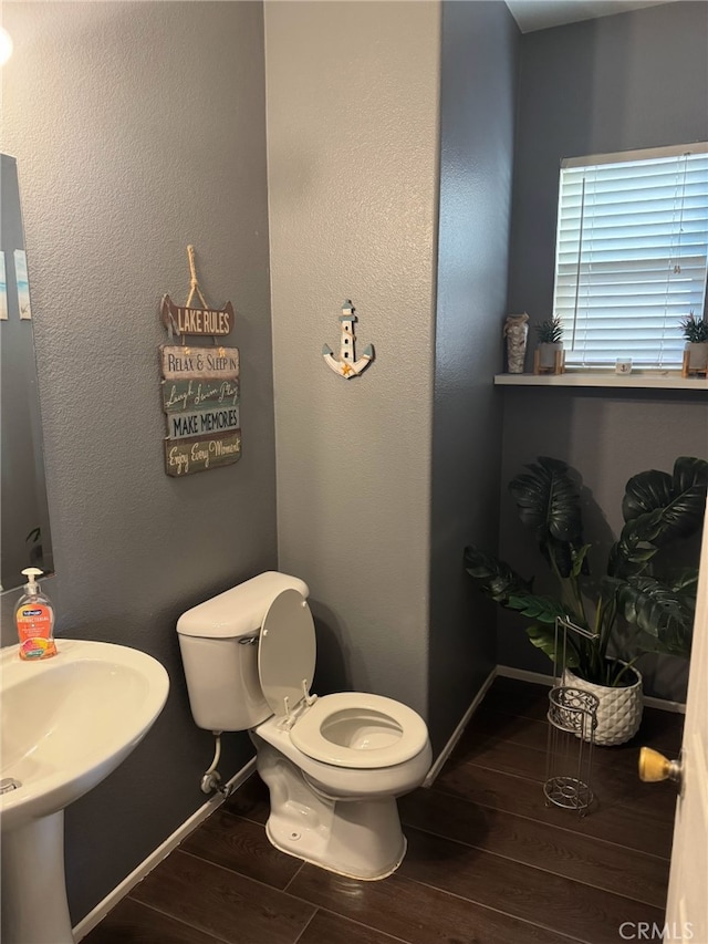 half bath with a sink, toilet, wood finished floors, and baseboards