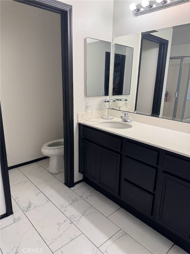 bathroom featuring marble finish floor, toilet, a shower with door, and vanity