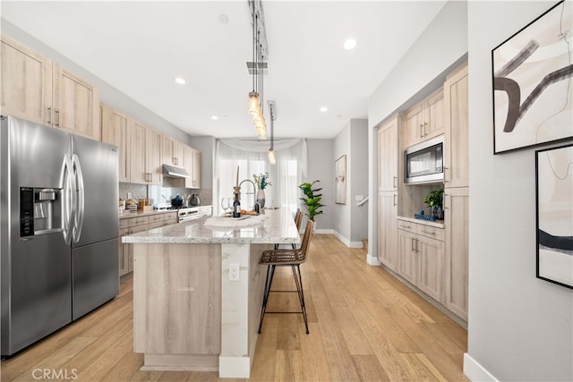 kitchen featuring appliances with stainless steel finishes, light brown cabinets, light wood finished floors, and tasteful backsplash