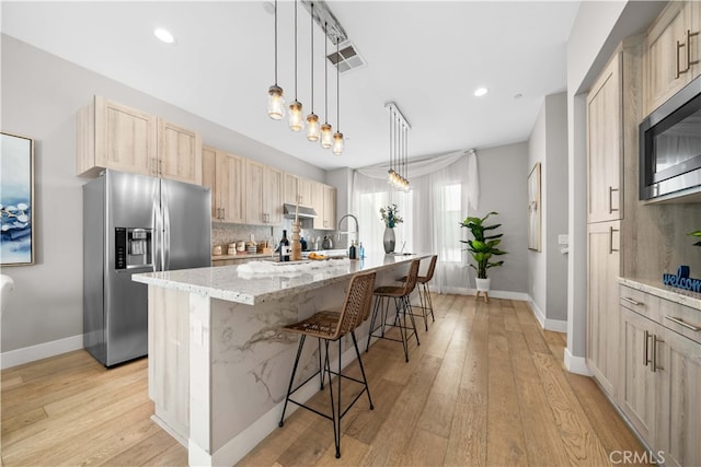 kitchen with light brown cabinets, a breakfast bar, visible vents, appliances with stainless steel finishes, and tasteful backsplash