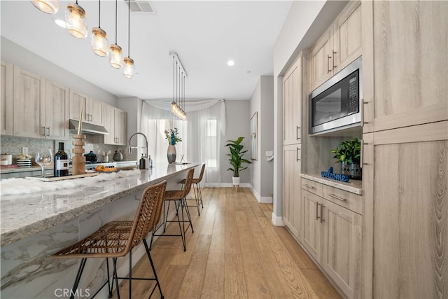 kitchen featuring tasteful backsplash, a breakfast bar area, built in microwave, under cabinet range hood, and a sink