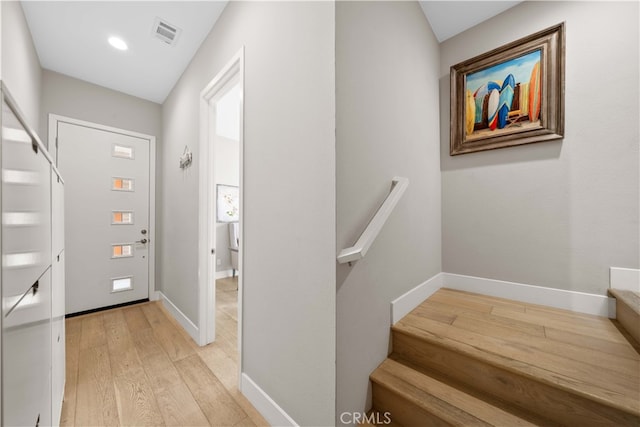 foyer entrance with light wood-type flooring, baseboards, stairs, and visible vents