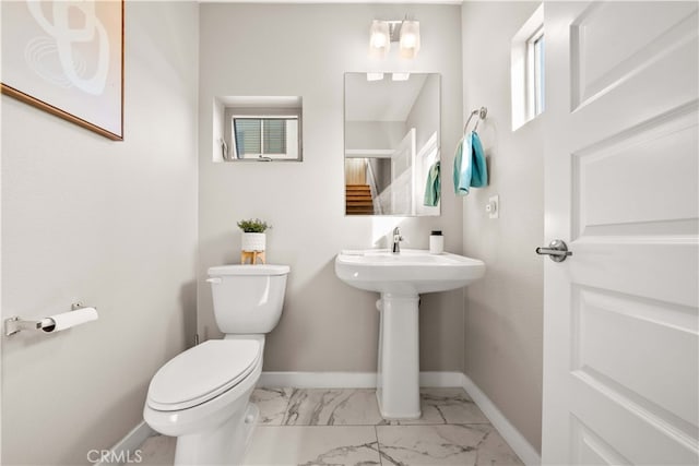 bathroom with marble finish floor, toilet, and baseboards