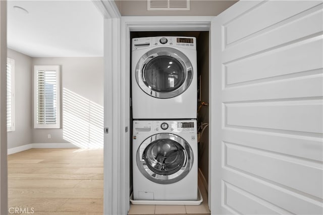 washroom with visible vents, light wood-style flooring, stacked washer / dryer, laundry area, and baseboards