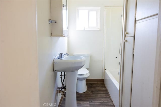 bathroom with a tub to relax in, wood finished floors, and toilet