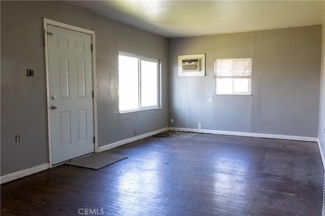 empty room with plenty of natural light, a wall unit AC, dark wood finished floors, and baseboards