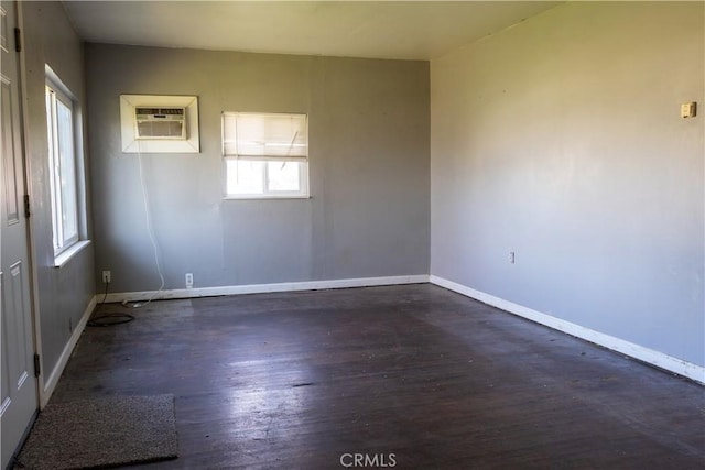 unfurnished room with baseboards, dark wood-type flooring, and a wall mounted air conditioner