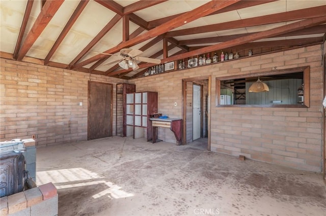 interior space with lofted ceiling with beams, ceiling fan, brick wall, a wood stove, and unfinished concrete floors