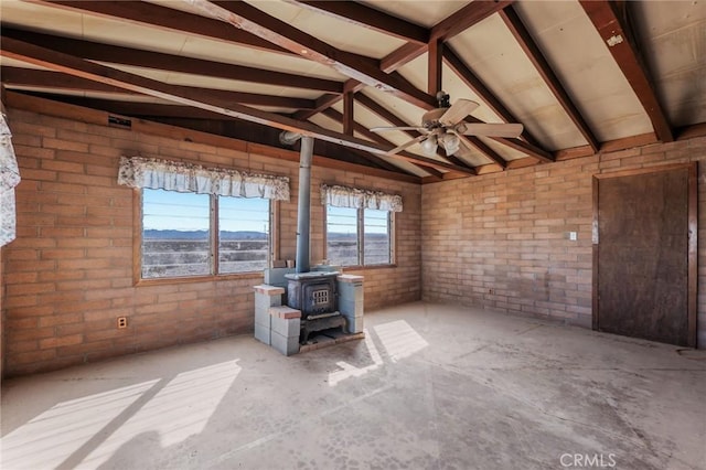 interior space featuring a ceiling fan, a wood stove, lofted ceiling with beams, and brick wall