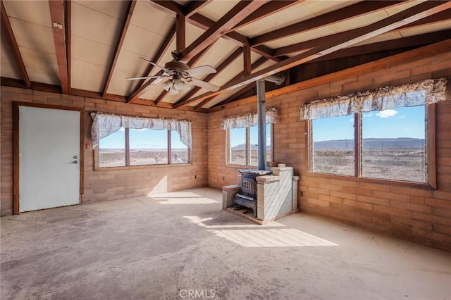 interior space with vaulted ceiling with beams, a wood stove, a mountain view, brick wall, and unfinished concrete floors