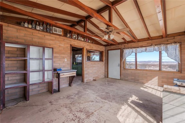 interior space featuring vaulted ceiling with beams, visible vents, ceiling fan, brick wall, and concrete flooring