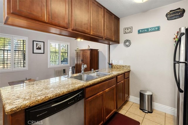 kitchen featuring brown cabinets, a peninsula, stainless steel appliances, a sink, and light tile patterned flooring