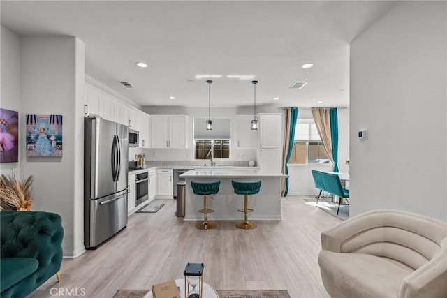 kitchen with a center island, decorative light fixtures, stainless steel appliances, light countertops, and white cabinetry