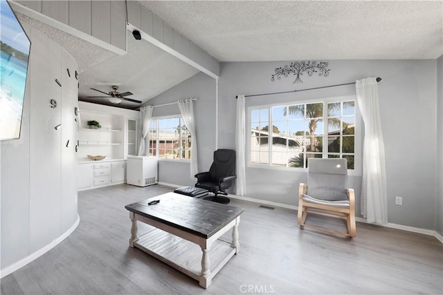 living area featuring visible vents, vaulted ceiling, a textured ceiling, wood finished floors, and baseboards