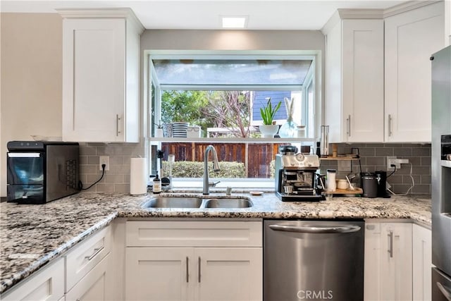 kitchen featuring white cabinets, dishwasher, backsplash, and a sink