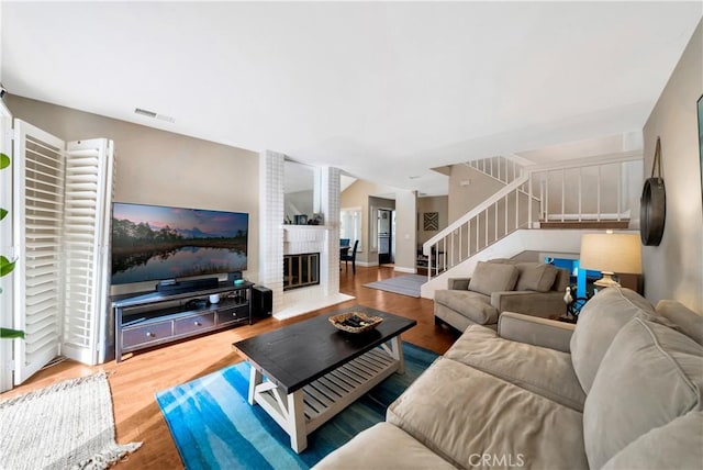 living area featuring a large fireplace, stairs, visible vents, and wood finished floors