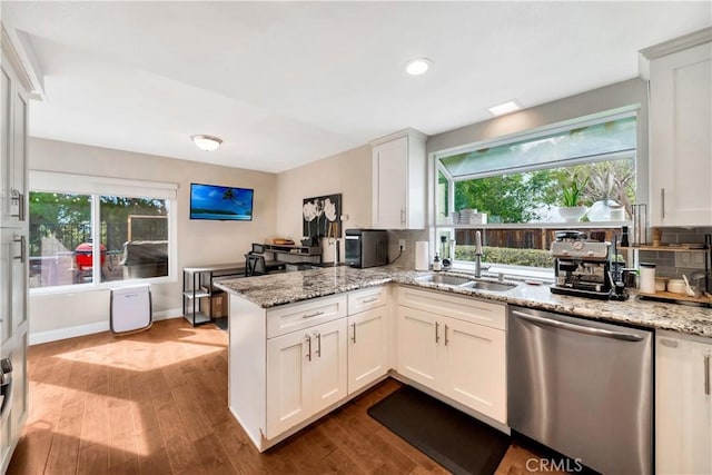 kitchen featuring plenty of natural light, dark wood-style flooring, a peninsula, stainless steel dishwasher, and a sink