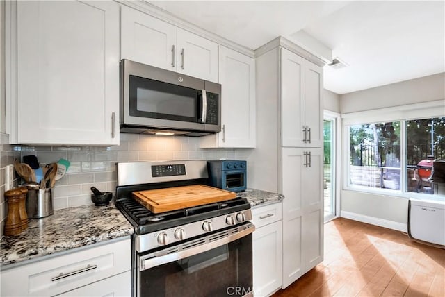 kitchen featuring stainless steel appliances, light stone counters, backsplash, and white cabinetry