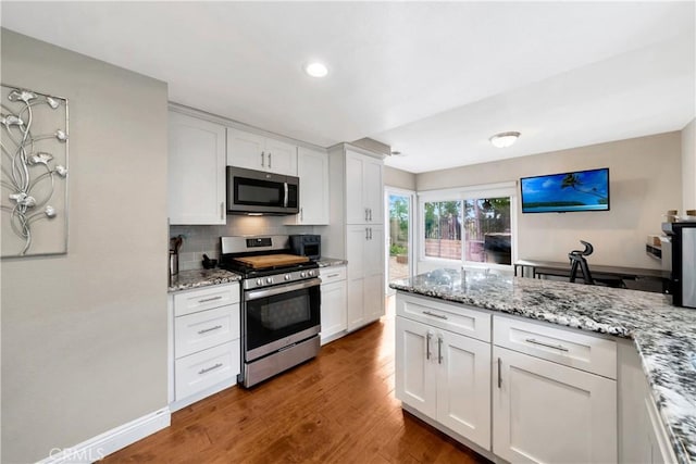 kitchen with stainless steel appliances, tasteful backsplash, white cabinets, and wood finished floors