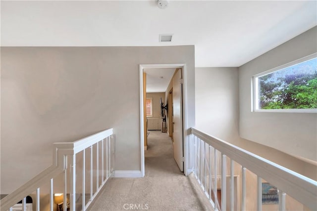 hall with baseboards, light carpet, visible vents, and an upstairs landing