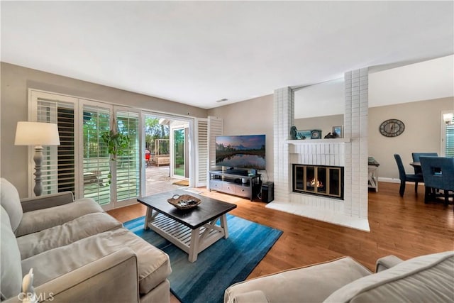 living room with a brick fireplace, visible vents, baseboards, and wood finished floors