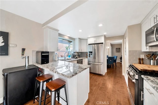 kitchen with a peninsula, appliances with stainless steel finishes, backsplash, and light stone counters