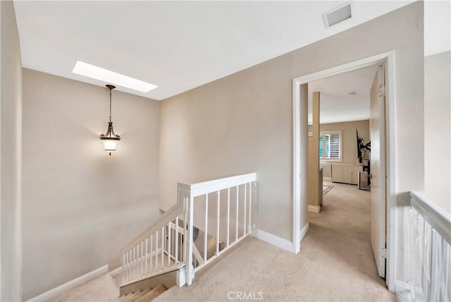 hallway featuring a skylight, visible vents, baseboards, an upstairs landing, and carpet floors