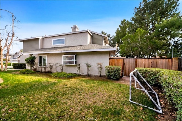 back of house with a yard, fence, a chimney, and stucco siding