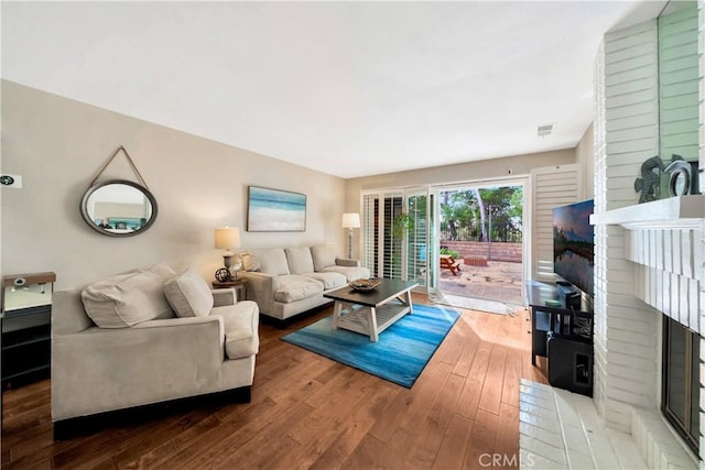 living room with a brick fireplace, visible vents, and hardwood / wood-style floors