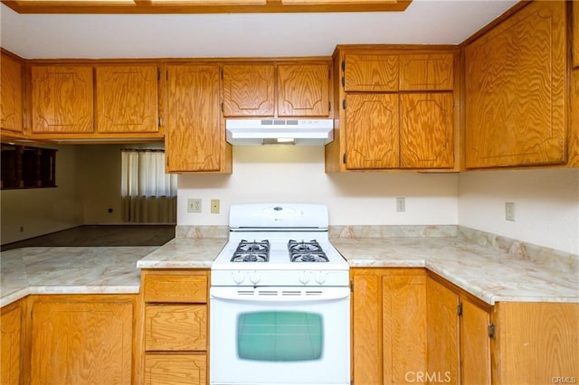 kitchen featuring under cabinet range hood, white range with gas stovetop, light countertops, and brown cabinetry