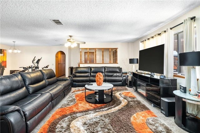 living room featuring arched walkways, a textured ceiling, ceiling fan with notable chandelier, visible vents, and carpet