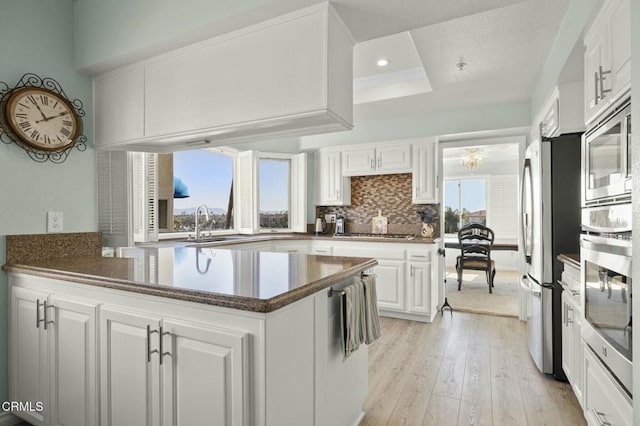 kitchen with backsplash, appliances with stainless steel finishes, white cabinets, light wood-type flooring, and a peninsula