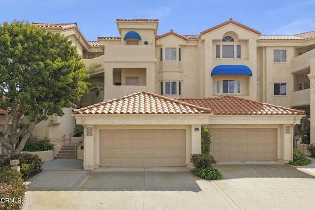 mediterranean / spanish-style home with a garage, a tile roof, driveway, and stucco siding