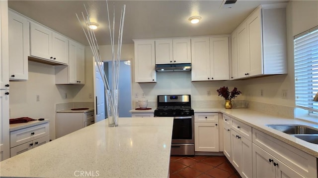 kitchen featuring light stone counters, stainless steel range with gas cooktop, visible vents, white cabinetry, and under cabinet range hood