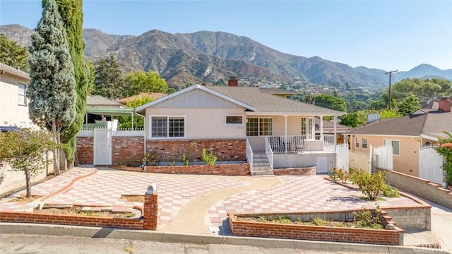 ranch-style home with a fenced front yard, a chimney, a mountain view, a porch, and brick siding