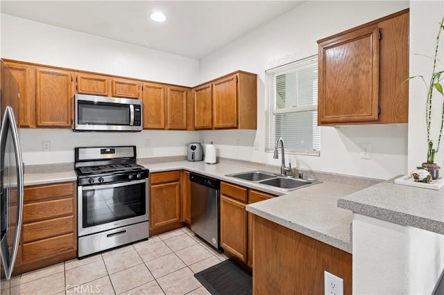 kitchen featuring a peninsula, appliances with stainless steel finishes, a sink, and brown cabinets