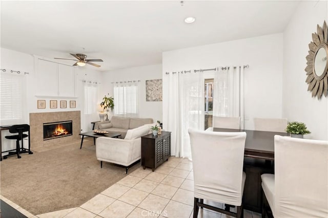 living area with light tile patterned floors, a tile fireplace, a ceiling fan, and light colored carpet