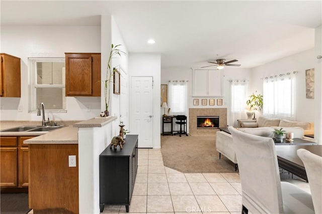 kitchen featuring light tile patterned floors, a warm lit fireplace, brown cabinetry, and a sink