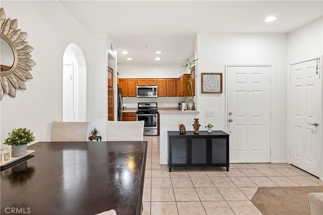 kitchen with arched walkways, light tile patterned floors, stainless steel appliances, light countertops, and brown cabinetry