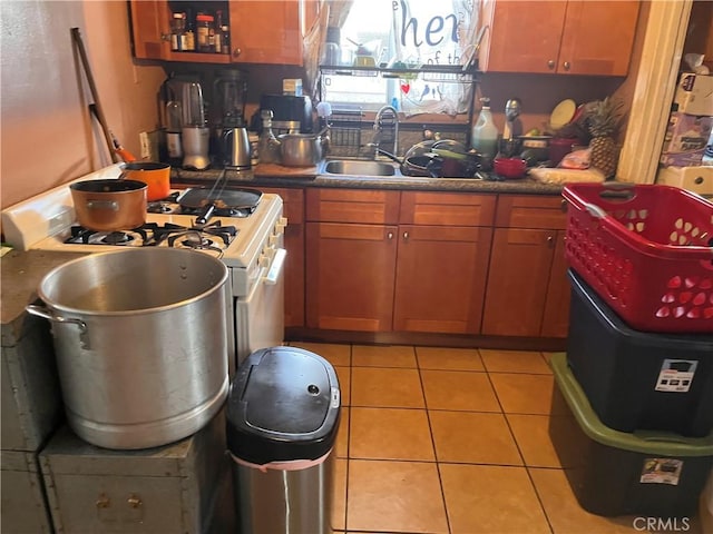 kitchen with light tile patterned floors, dark countertops, brown cabinets, white gas stove, and a sink