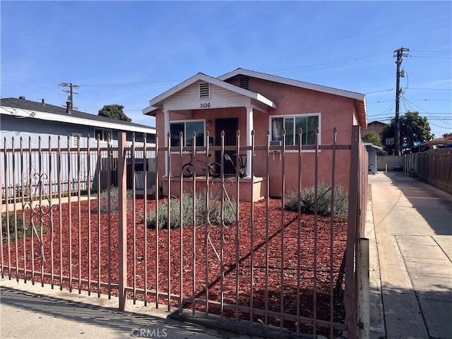 bungalow featuring a fenced front yard and stucco siding