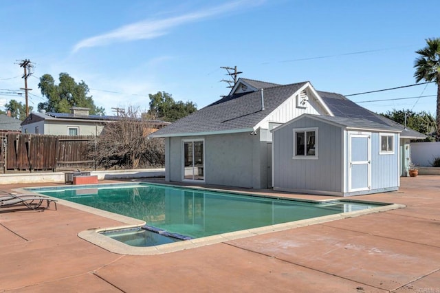 view of pool featuring a patio area, a pool with connected hot tub, fence, and an outbuilding