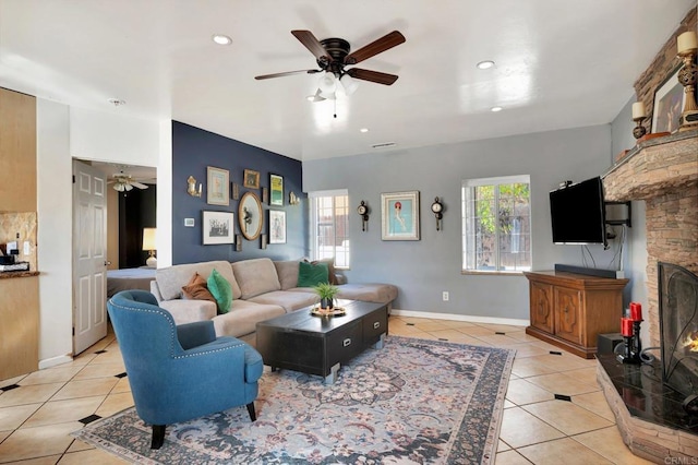 living room with a warm lit fireplace, light tile patterned floors, a ceiling fan, and baseboards