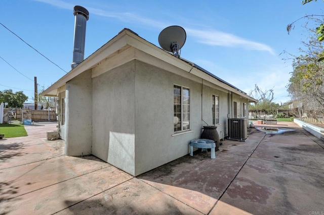 view of property exterior with central air condition unit, stucco siding, fence, and a patio