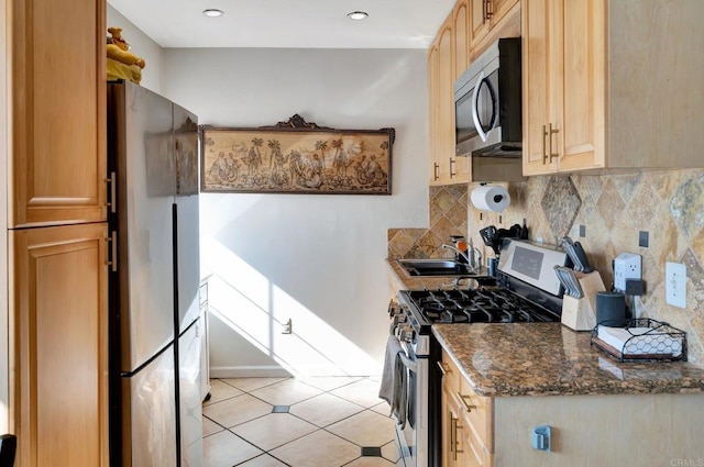 kitchen with stainless steel appliances, tasteful backsplash, light brown cabinetry, a sink, and dark stone counters