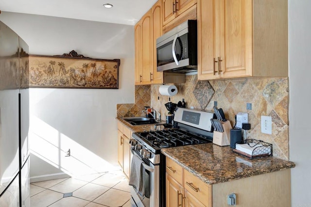 kitchen featuring stainless steel appliances, light brown cabinets, a sink, and backsplash