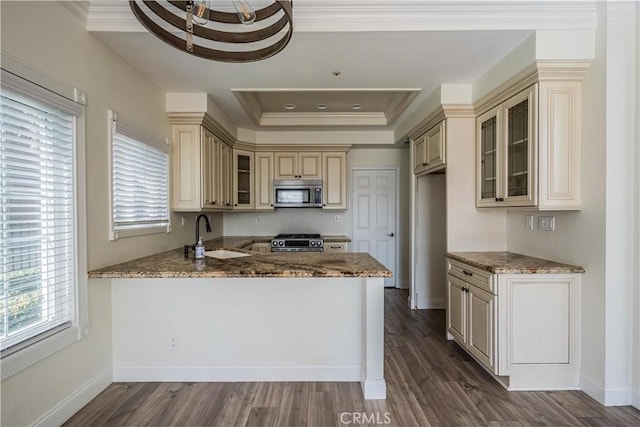 kitchen featuring glass insert cabinets, appliances with stainless steel finishes, light stone countertops, cream cabinetry, and a sink