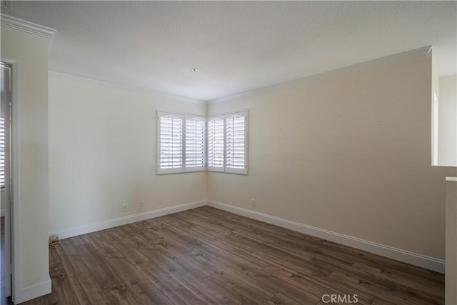 spare room with crown molding, dark wood finished floors, and baseboards